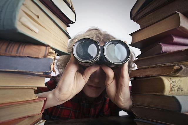Person peering through binoculars between books, symbolizing deep search and discovery